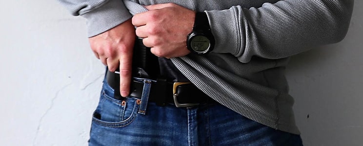 A concealed carrier lifting up their shirt with one hand, the other hand on their pistol. The belt holds firm as they lift the pistol from its holster.